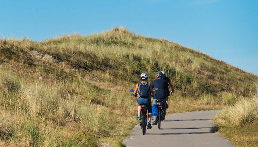 Zwei Radfahrer auf Dünenweg auf Sylt zwischen Graslandschaft und blauem Himmel.