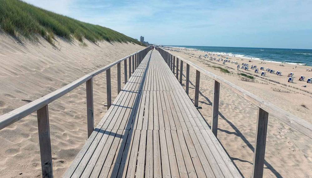 Ein Holzsteg führt durch die Dünenlandschaft auf Sylt in Richtung Nordseestrand.