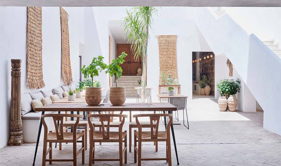 Large wooden table and chairs decorated with plants in the stylish and sunny courtyard of the Barefoot Hotel Mallorca.