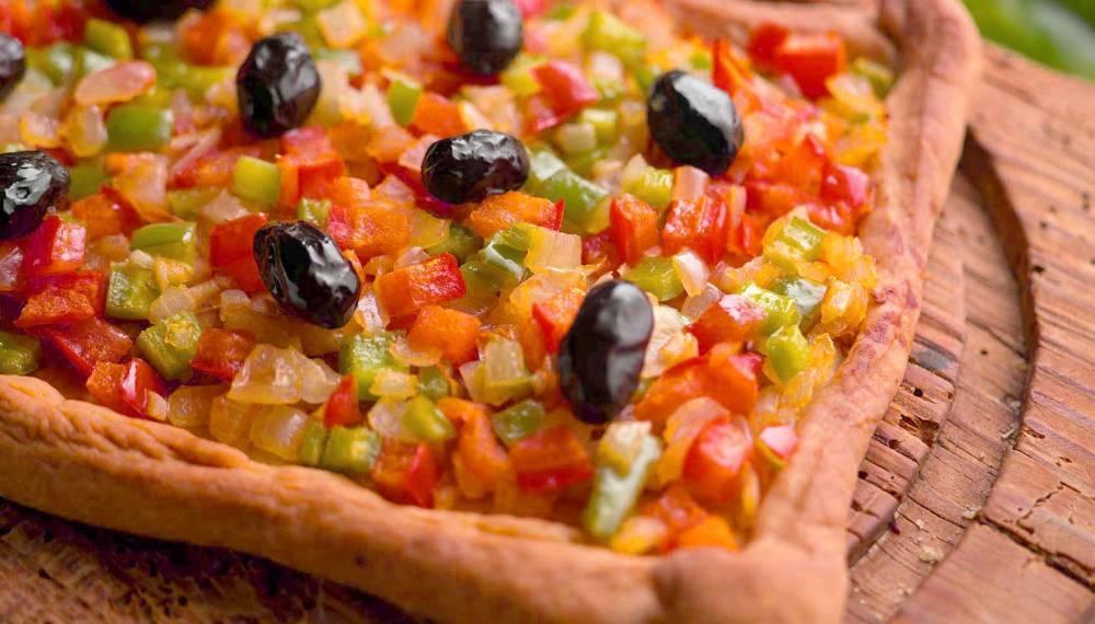 Traditionelle mallorquinische Gemüsepizza Coca de Verdura mit Oliven und frischen Zutaten, serviert rustikal