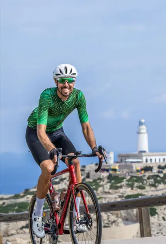 Radfahrer auf einer sonnigen Küstenstraße auf Mallorca mit Meer und Bergen im Hintergrund