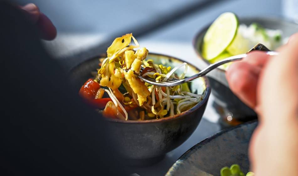 Close-up of a fork picking up fresh sprouts and vegetables from a bowl, served at #herrhoshi by the Baltic Sea.