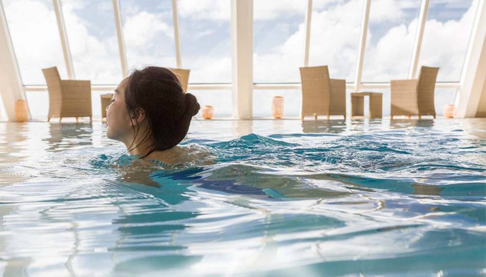 Eine Frau schwimmt im Pool des Wellnessbereichs im Wyn. Strandhotel auf Sylt, mit atemberaubendem Panoramablick.