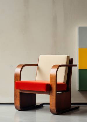 Detailaufnahme eines Stuhls aus der Bauhaus-Ära, rotes Polster und Holzrahmen, vor moderner Wandkunst im Museum in Weimar