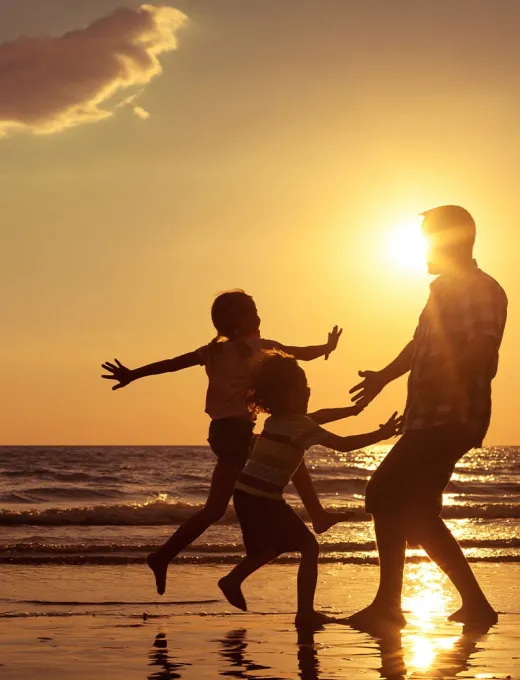 Family playing on the beach in the sunset, two children running towards their father.