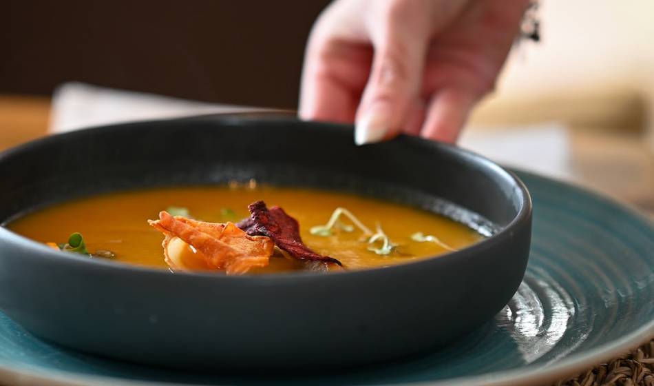 A black bowl of soup decorated with crispy vegetable toppings on a blue plate at Barefoot Restaurant Mallorca.