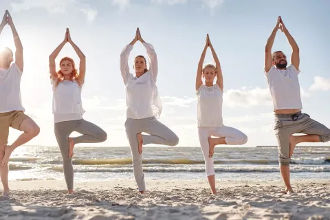 Eine Gruppe von Menschen beim Yoga am Strand von Rügen, mit Blick auf die Ostsee und strahlendem Sonnenschein