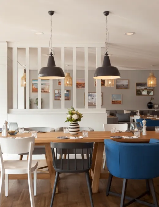 Helles Restaurant mit Holztisch, blauen und grauen Sesseln, Pendelleuchten und Blumendeko im Wyn. Strandhotel Sylt