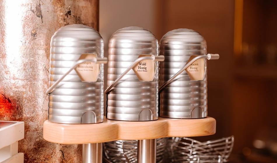 Three metal honey dispensers with different types, including forest and blossom honey, on a wooden stand in #fraukorn.