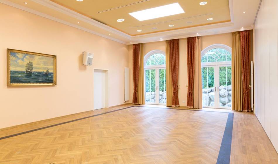 Large, bright event room in the Vju Hotel on Rügen with wooden floors, large windows and subtle wall decoration, ideal for events.