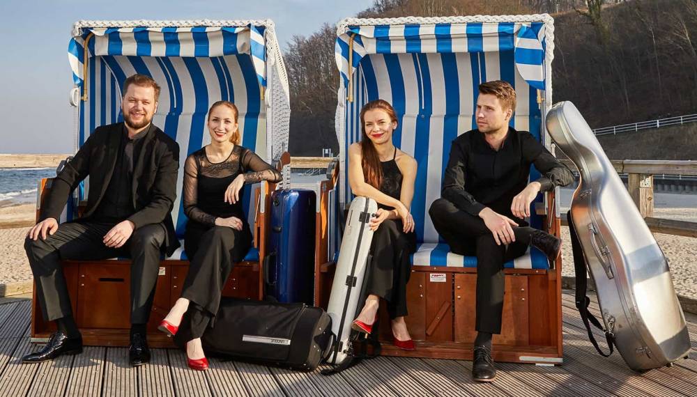 Arminda Quartett sitzt in Strandkörben am Ostseestrand mit Instrumentenkoffern und Reisegepäck.