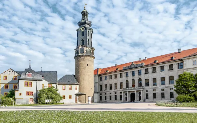 Das Stadtschloss Weimar bei sonnigem Wetter. Kleine Schäfchenwolken am Himmel und blühender Klee auf dem Rasen davor.