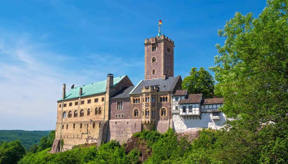 Porträt der historischen Wartburg mit romanischer Architektur, Wachturm und Wald im Vordergrund bei sonnigem Wetter