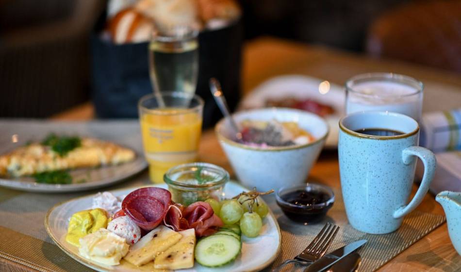 Richly laid breakfast table in the Vju Hotel Rügen with a cheese plate, sausage, fruit, yoghurt and coffee.