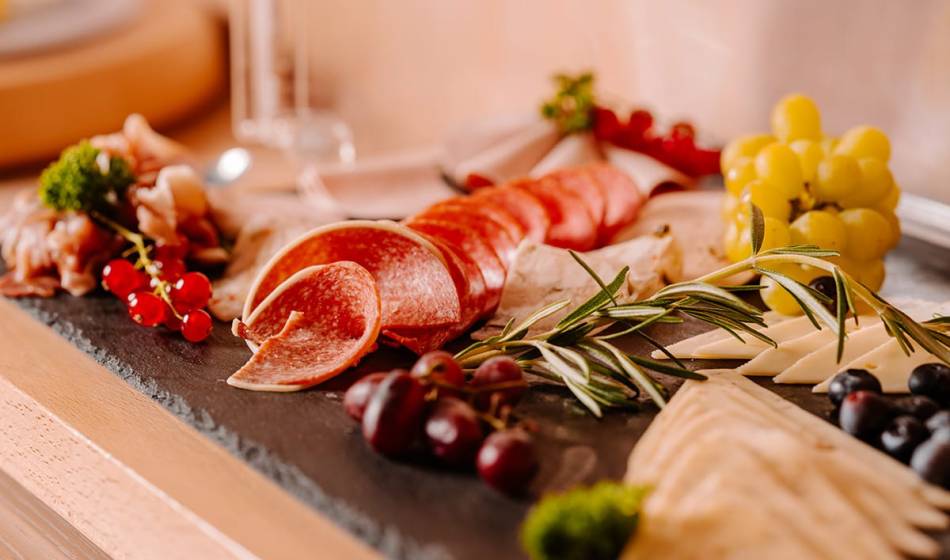 Slate plate decorated with a selection of cheese, cold cuts, grapes and rosemary, served at #fraukorn in the Hotel Seezeichen.