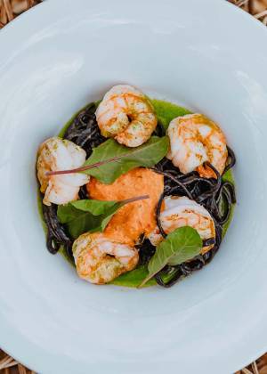 Köstliches Gericht mit gegrillten Garnelen, schwarzer Tintenfischpasta, grüner Sauce und frischen Kräutern im Kaiserhof
