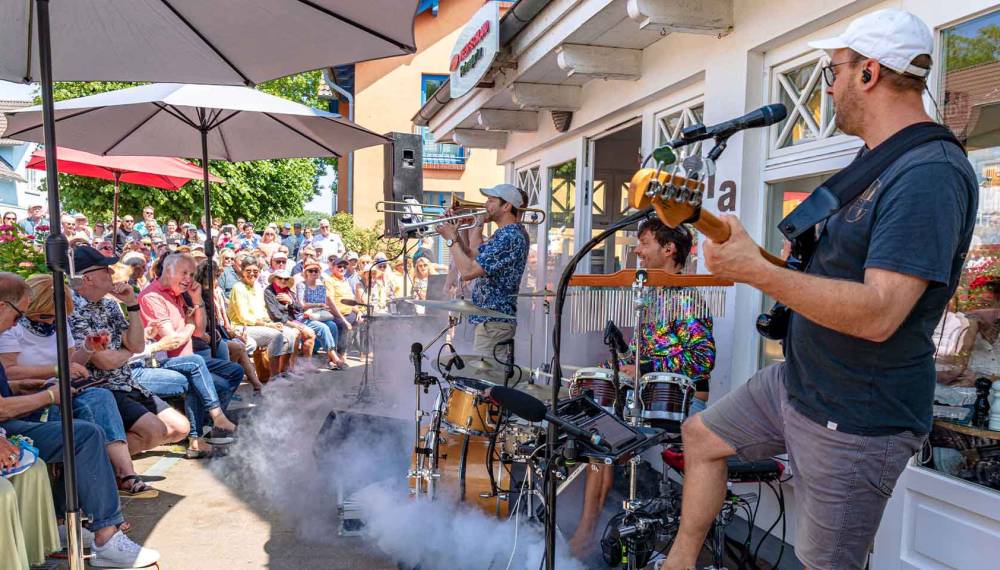 Eine Band spielt beim Jazzfest Ahrenshoop vor einem Geschäft, drumherum haben sich Menschen versammelt.