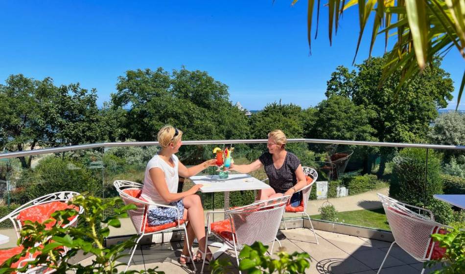 Two women enjoy cocktails on the terrace of Kaiserhof Heringsdorf on Usedom with a view of the Baltic Sea and a relaxed summer atmosphere.