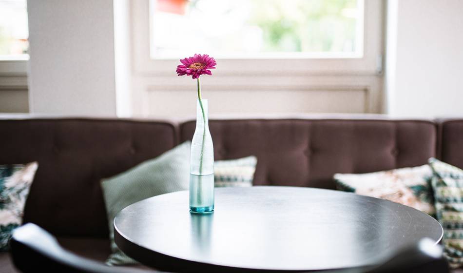 Close-up of a round table with a vase and a single flower in the Café #faukorn of the Hotel Künstlerquartier Seezeichen.