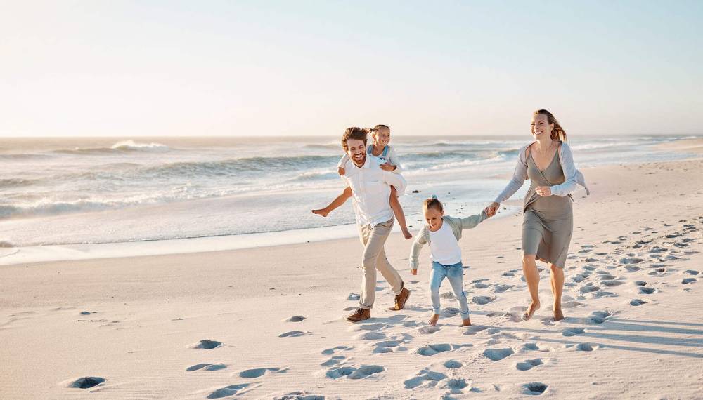 Fröhliche Familie spielt mit zwei Kindern am Strand von Rügen, alle lachen und genießen den Moment.