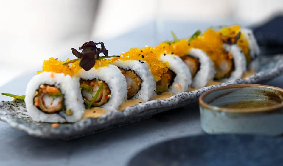 Close-up of American sushi rolls filled with tempura and vegetables, decorated with fish roe and herbs in #herrhoshi.