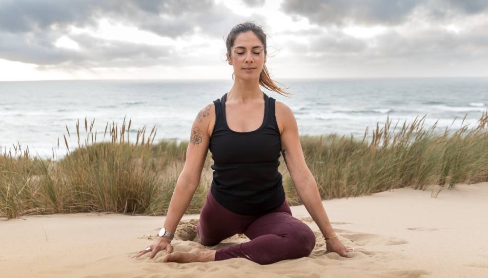 Yogalehrerin Halima Elkasmi in einer Meditationshaltung am Strand bereit für das Yoga Retreat im Vju Hotel auf Rügen.