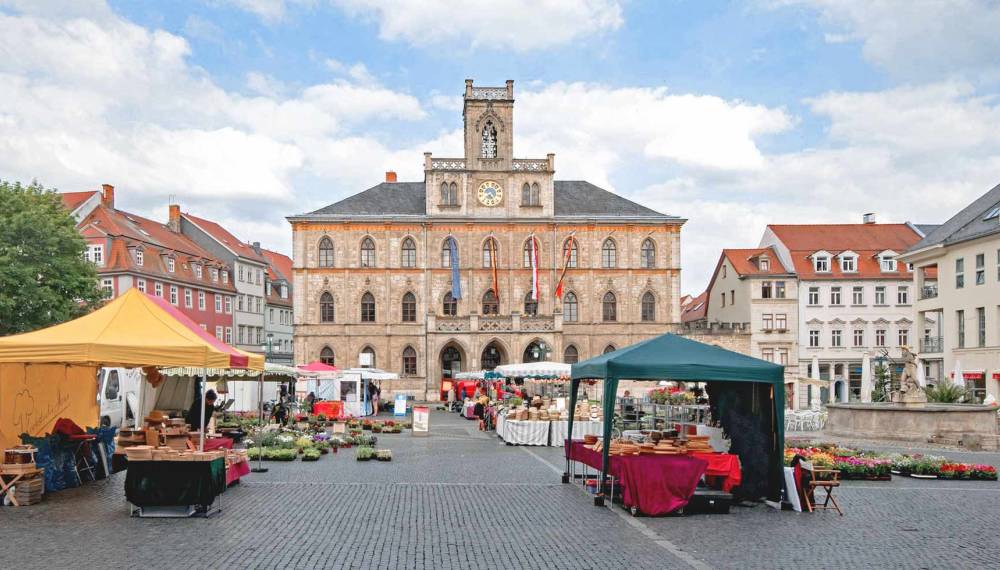 Marktplatz in Weimar mit historischem Rathaus, Marktständen und umliegenden Bürgerhäusern.