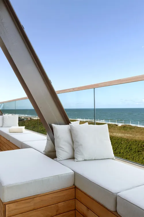 Modern roof terrace with white seating cushions and views of the sea and dunes in the background.