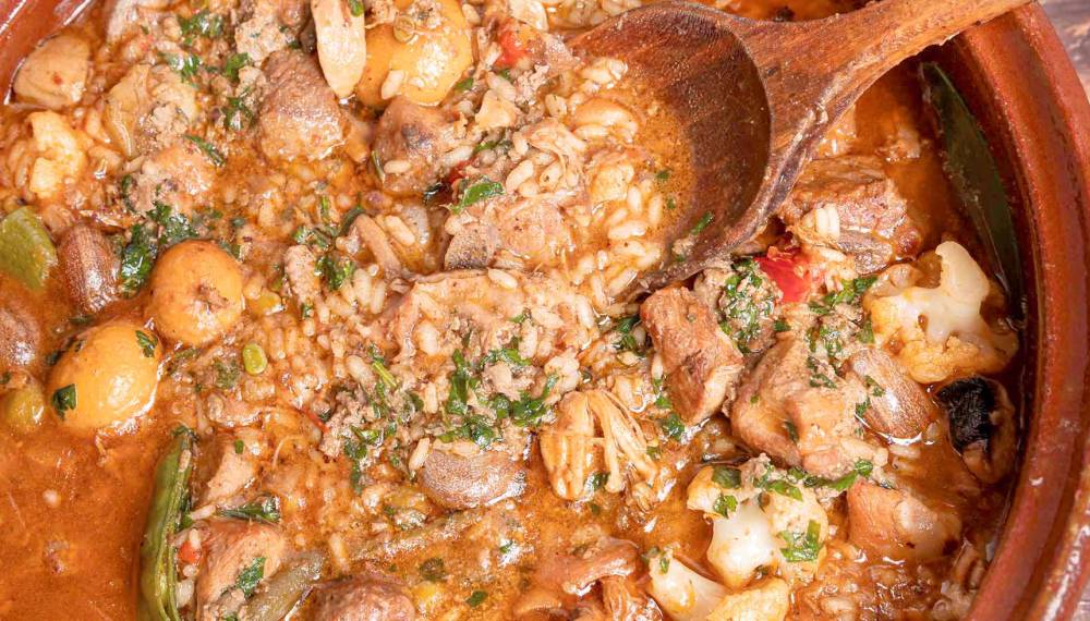 Nahaufnahme eines traditionellen Arròs Brut mit Fleisch, Gemüse und Reis in einer Tonschale, typisch mallorquinisch