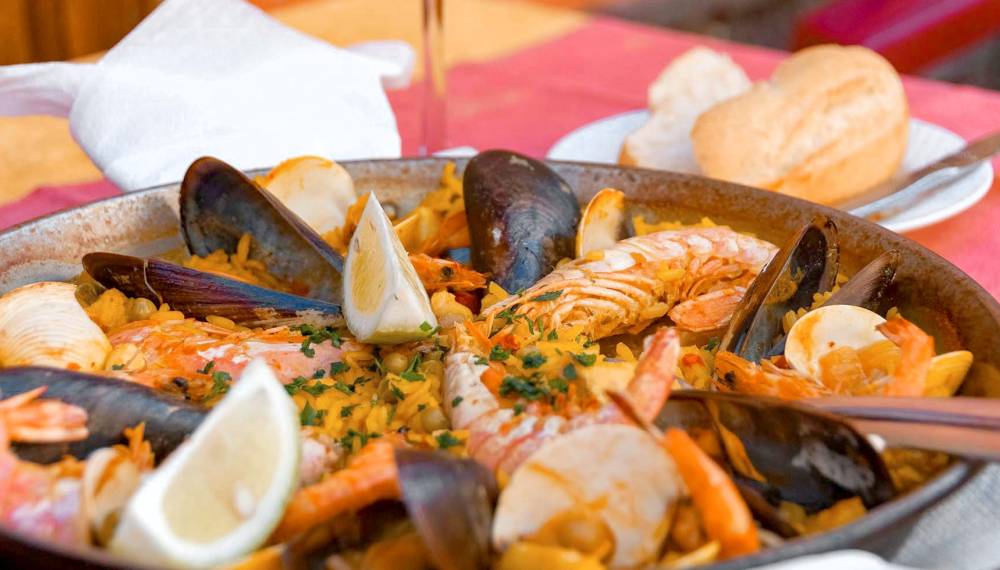 Eine reichhaltige Paella mit Garnelen, Muscheln und Zitronenspalten in einer traditionellen Pfanne serviert