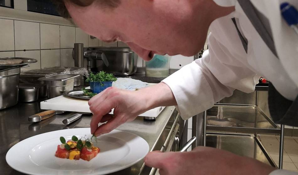 Head chef of the Vju Hotel on Rügen prepares an artistic dish on a white plate with precision.