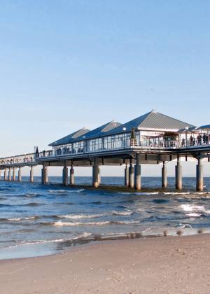 Die Heringsdorfer Seebrücke, umgeben von Wellen und einem klaren blauen Himmel, aufgenommen vom Sandstrand des Seeheilbades