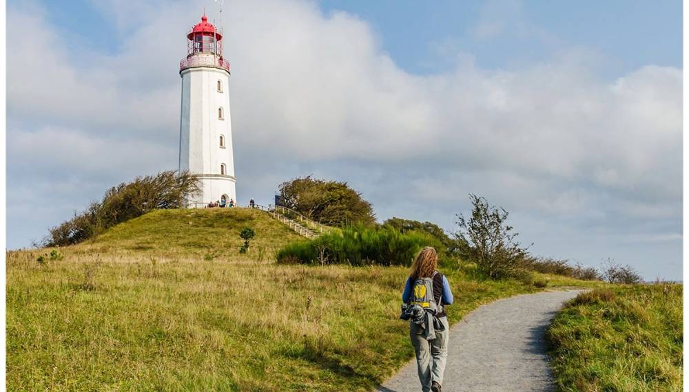 Frau wandert auf Weg durch Dünenlandschaft zum Leuchtturm Dornbusch auf Hiddensee