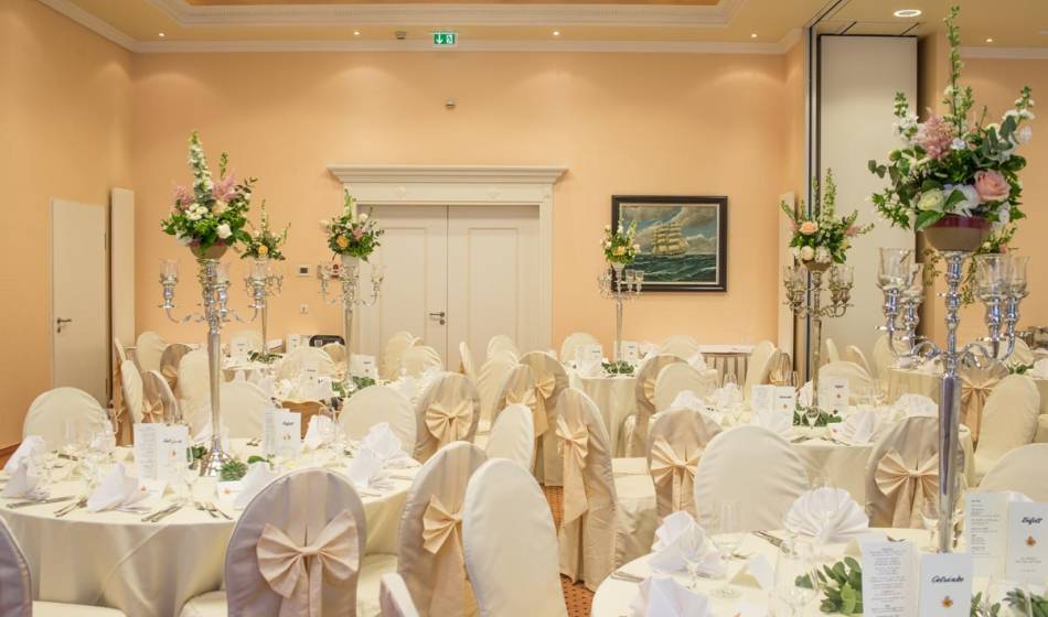 Festively decorated wedding hall in the Vju Hotel on Rügen, with round tables, candlesticks and flower arrangements.