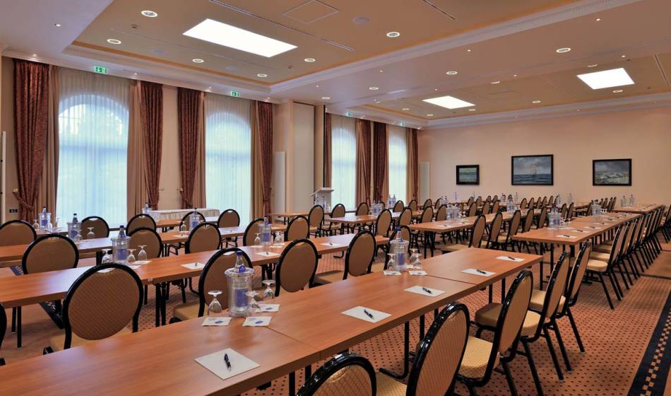 Spacious meeting room in the Vju Hotel on Rügen, with long tables, chairs, water bottles and writing materials, ideal for conferences.