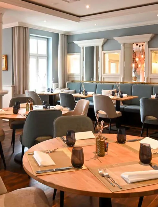 Blick in das maritime Restaurant Küstensilber mit hellen Stühlen und Bänlen, Holzdekor und eingedeckten Tischen im Vju Hotel auf Rügen.