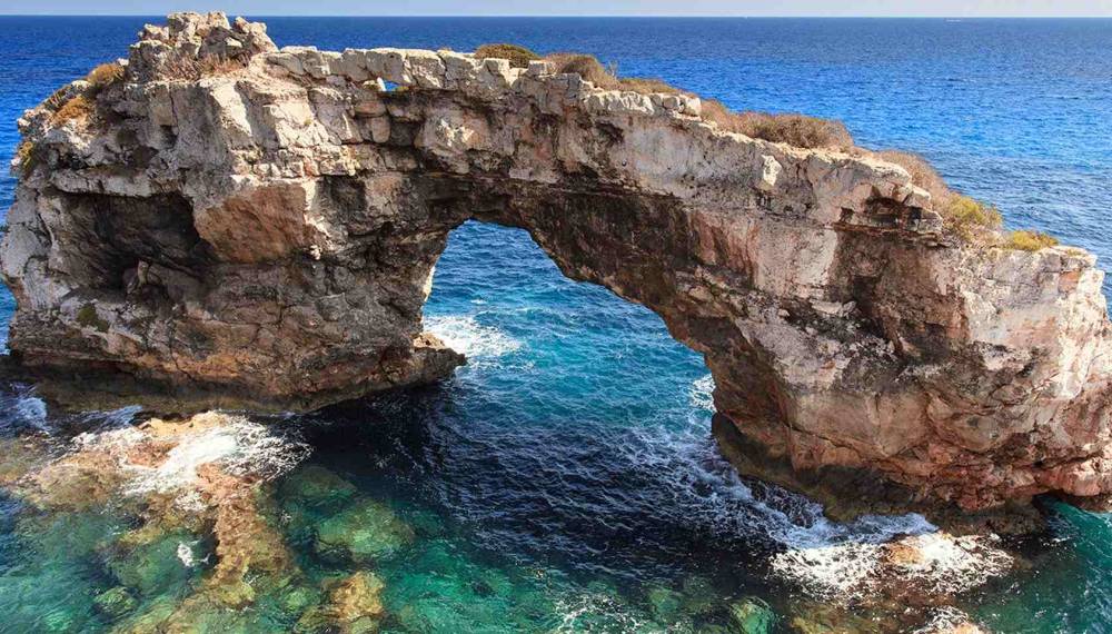 Natürlicher Felsbogen an der Cala Santanyí auf Mallorca über klarem blauem Meer.