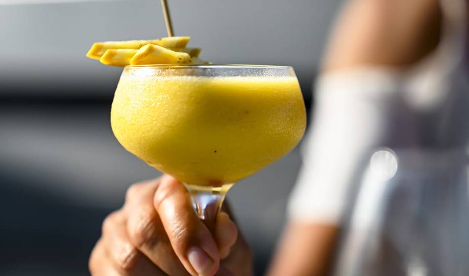 Yellow cocktail in a cocktail glass, garnished with fresh fruits and held by a hand at #herrhoshi in Ahrenshoop.