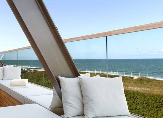 Moderne Terrasse des Wyn Strandhotels Sylt mit weißen Sitzpolstern und Blick auf das Meer und Dünen.
