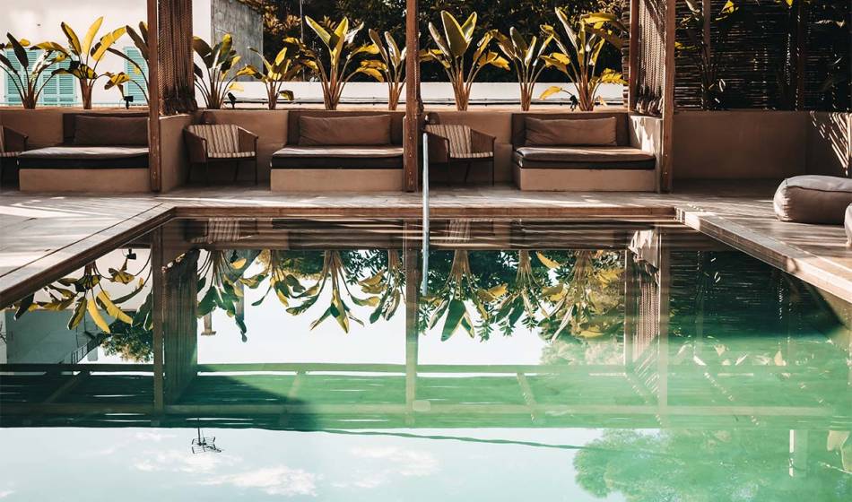 Outdoor area with pool, surrounded by palm trees and loungers in the wellness area of ​​the Barefoot Hotel Mallorca.