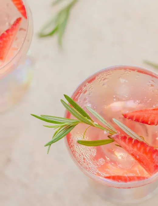 Glass with sparkling summer drink, decorated with fresh strawberries and rosemary, refreshing look.