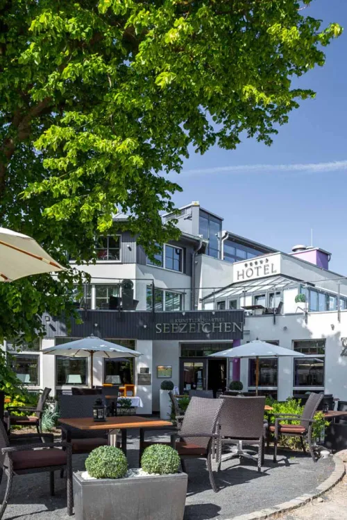 Sunny terrace of the Seezeichen artist quarter in Ahrenshoop with seating and green surroundings.