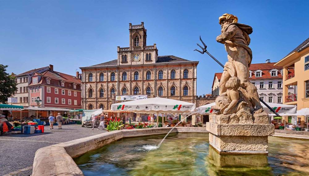 Porträt des Weimarer Marktplatzes mit Rathaus, Brunnenfigur im Vordergrund, Gastronomiezelten und historischen Häusern