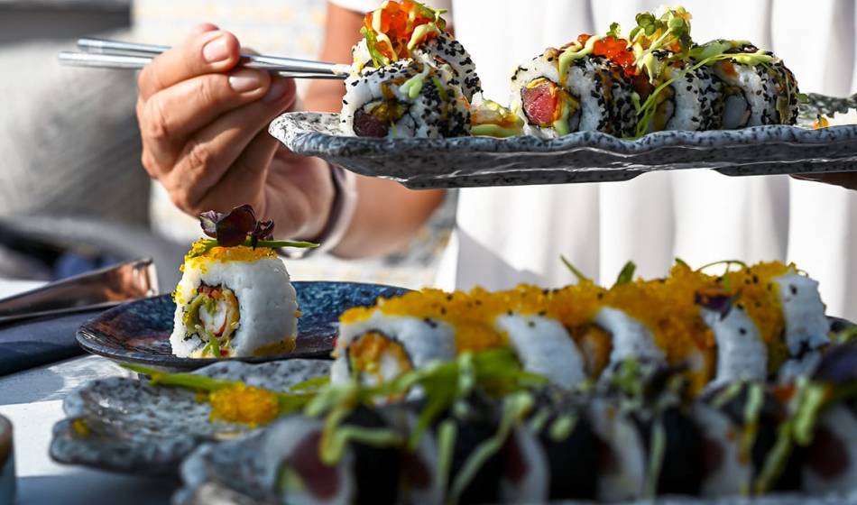 Hand with a plate full of fresh sushi in front of other carefully arranged sushi variations in the #herrhoshi restaurant in Ahrenshoop.