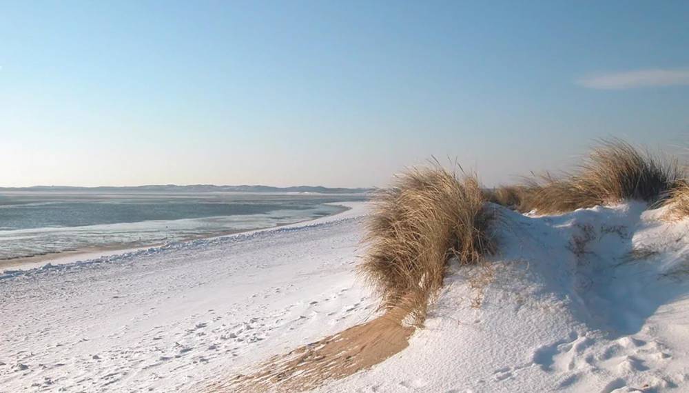 Verschneiter Strand und Dünen von Sylt, mit Blick auf das ruhige Meer zum Adventsspecial Angebot im Wyn. Strandhotel.