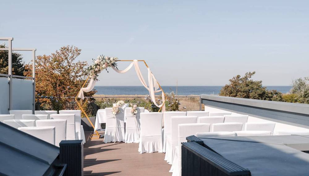 Trautisch auf der Seezeichen-Terrasse mit Blumenbogen, Meerblick und Bestuhlung für eine kleine Hochzeitsgesellschaft.