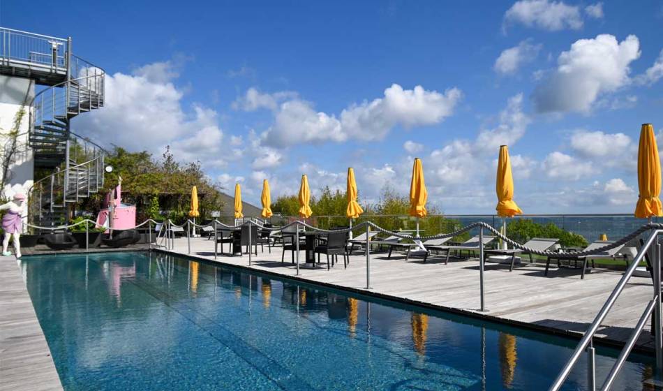 Kaiserhof Heringsdorf's outdoor pool with loungers, parasols and views of the blue sky and sea.