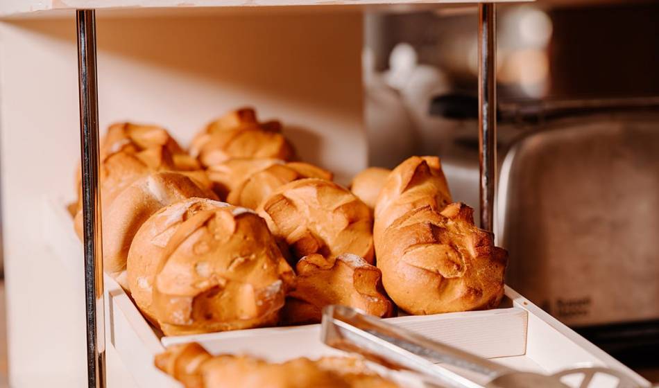 Freshly baked, golden-brown rolls in a white wooden box, served with silver tongs at the Künstlerquartier Seezeichen.