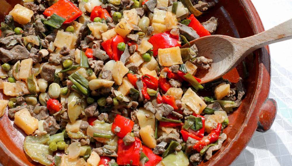 Traditionelles Frito Mallorquín in einer Tonpfanne, mit frischem Gemüse und Fleisch angerichtet
