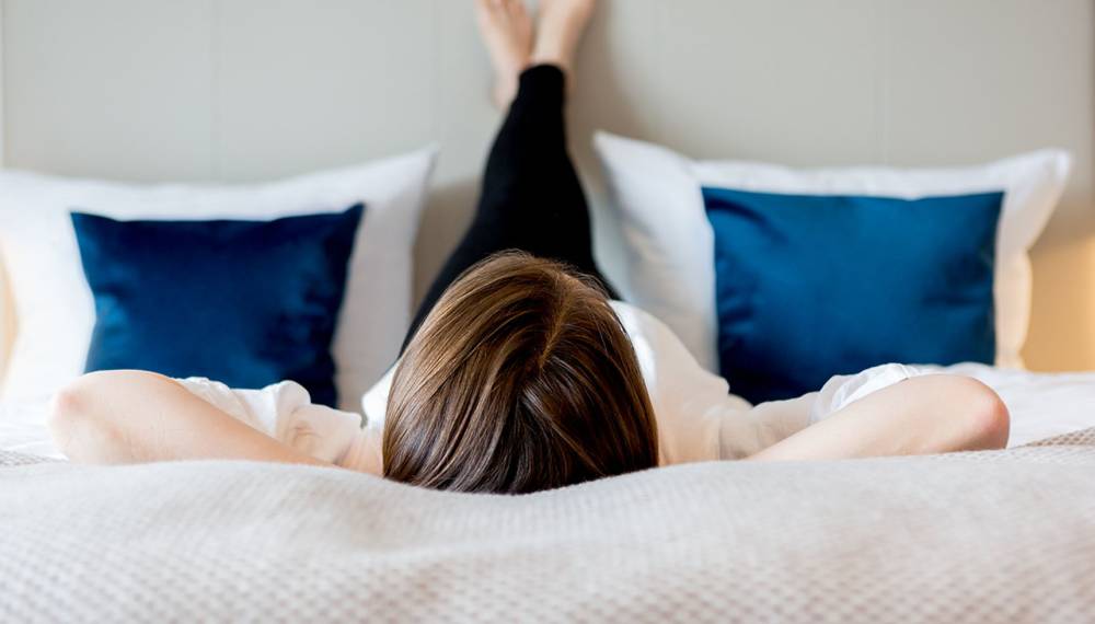 Frau liegt entspannt auf dem Bett mit blauen Kissen im Hotelzimmer des Koopmanns Hotel und Lädchen.